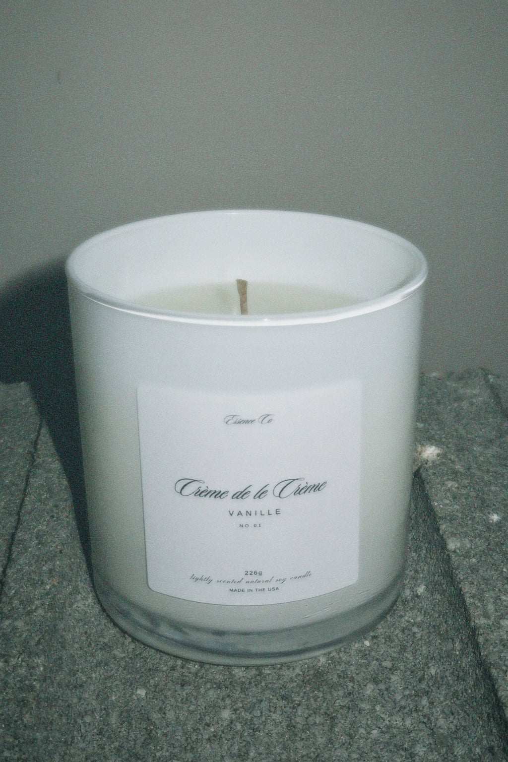 White candle in a glass container with a label on a gray surface