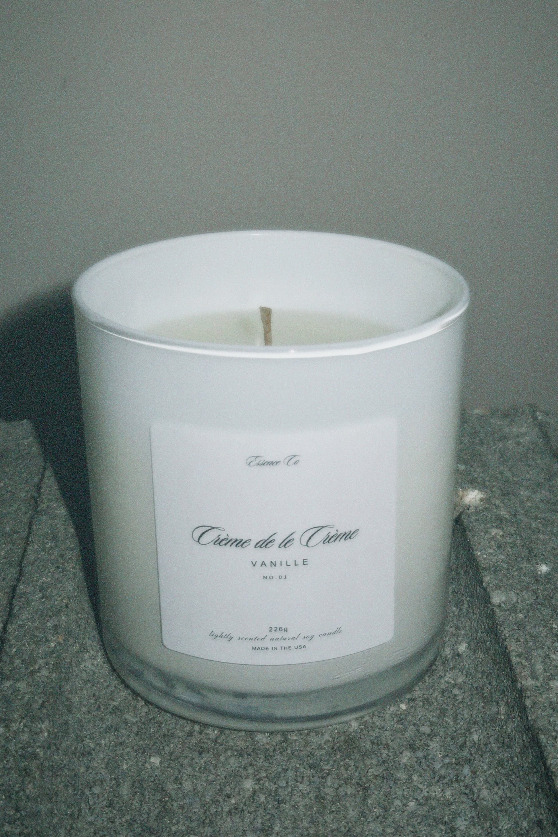 White candle in a glass container with a label on a gray surface