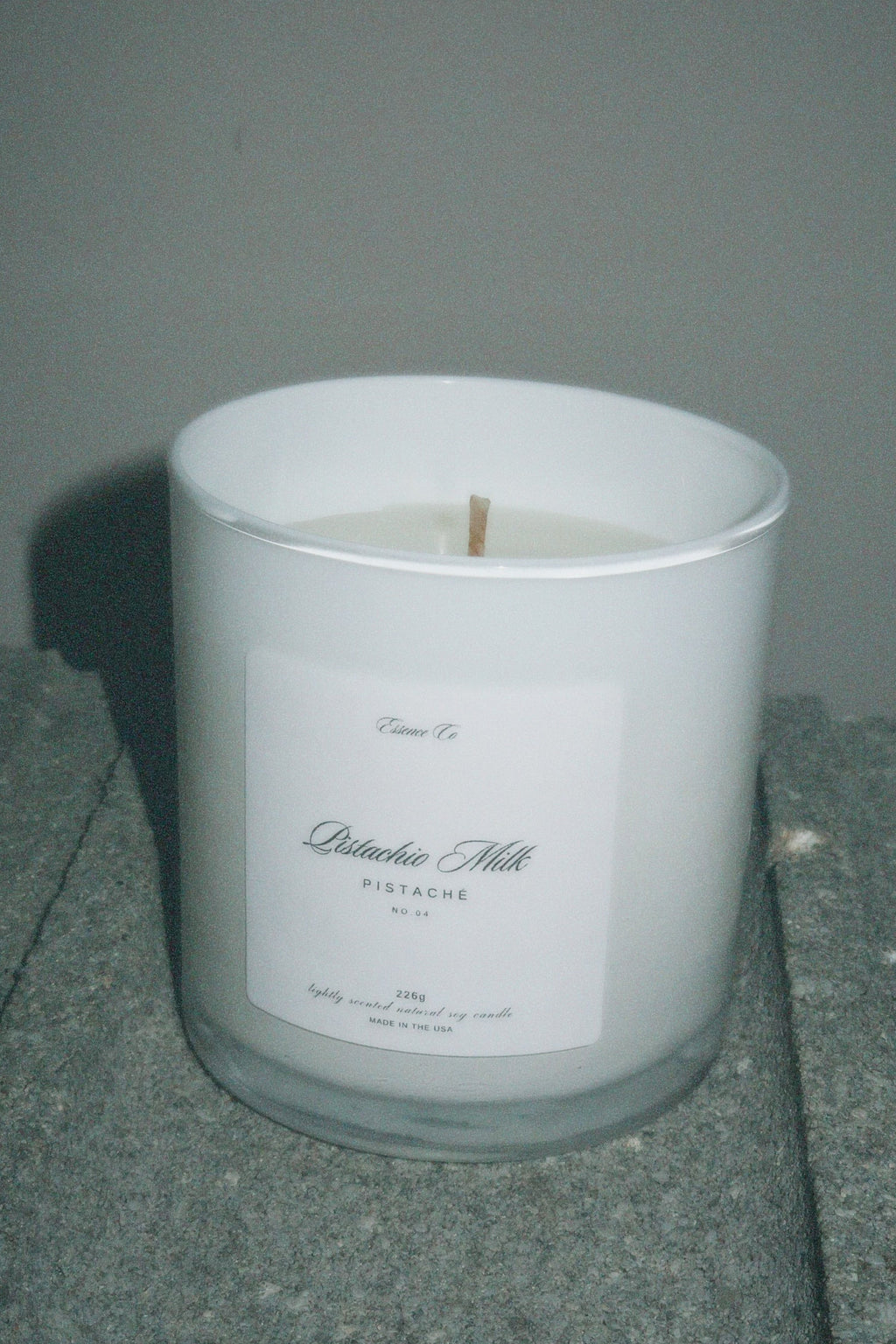 White candle in a glass container with a label on a gray surface