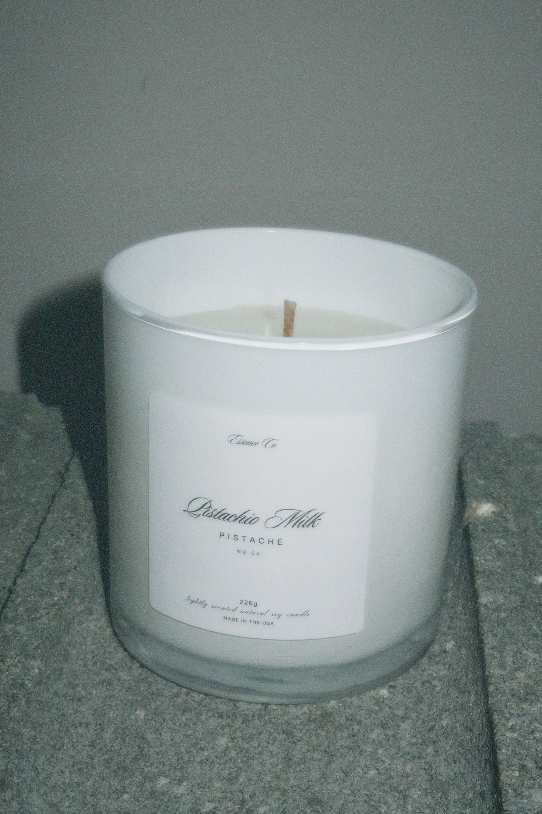 White candle in a glass container with a label on a gray surface
