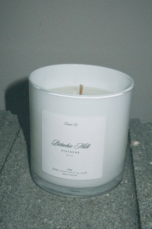 White candle in a glass container with a label on a gray surface