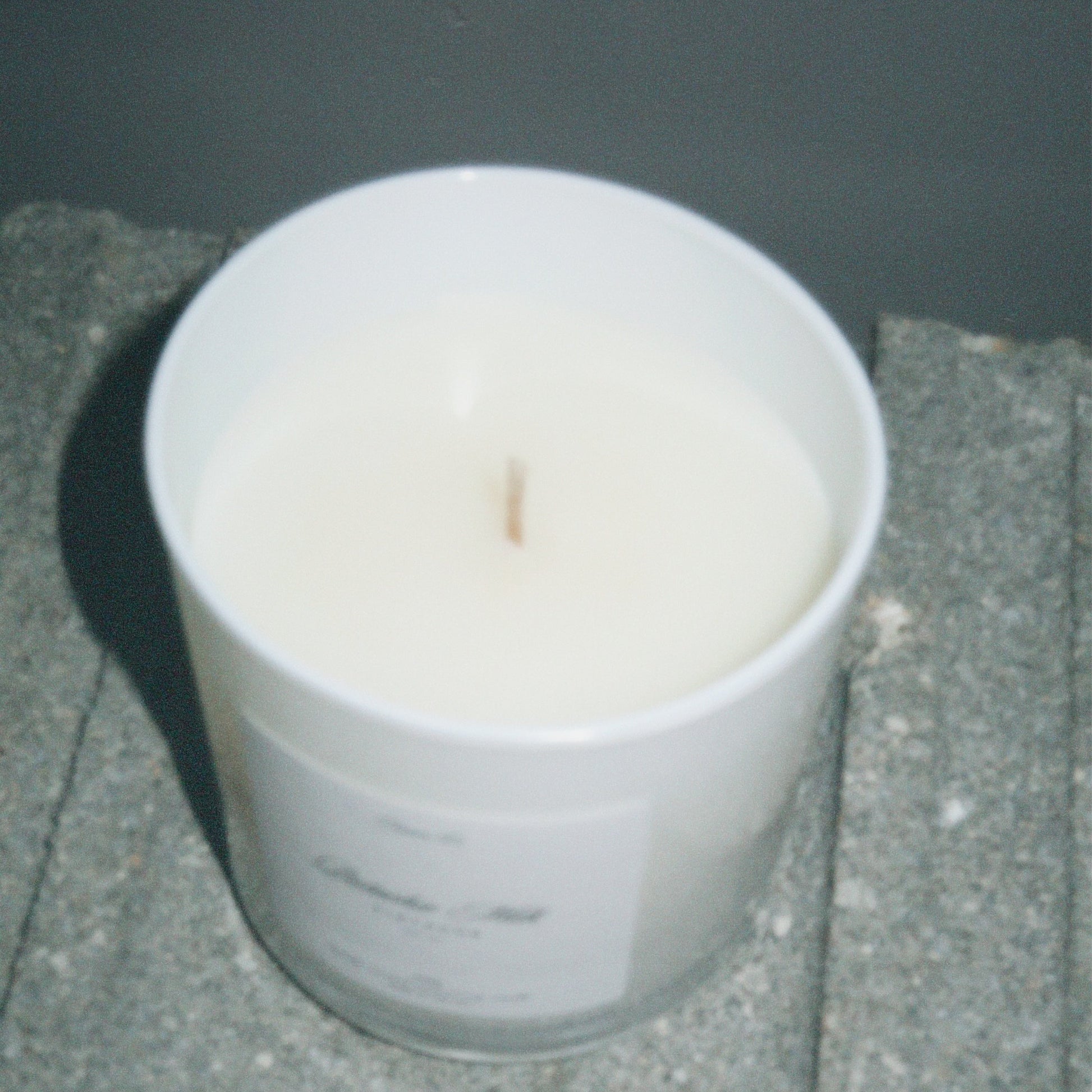 White candle in a glass container on a stone surface