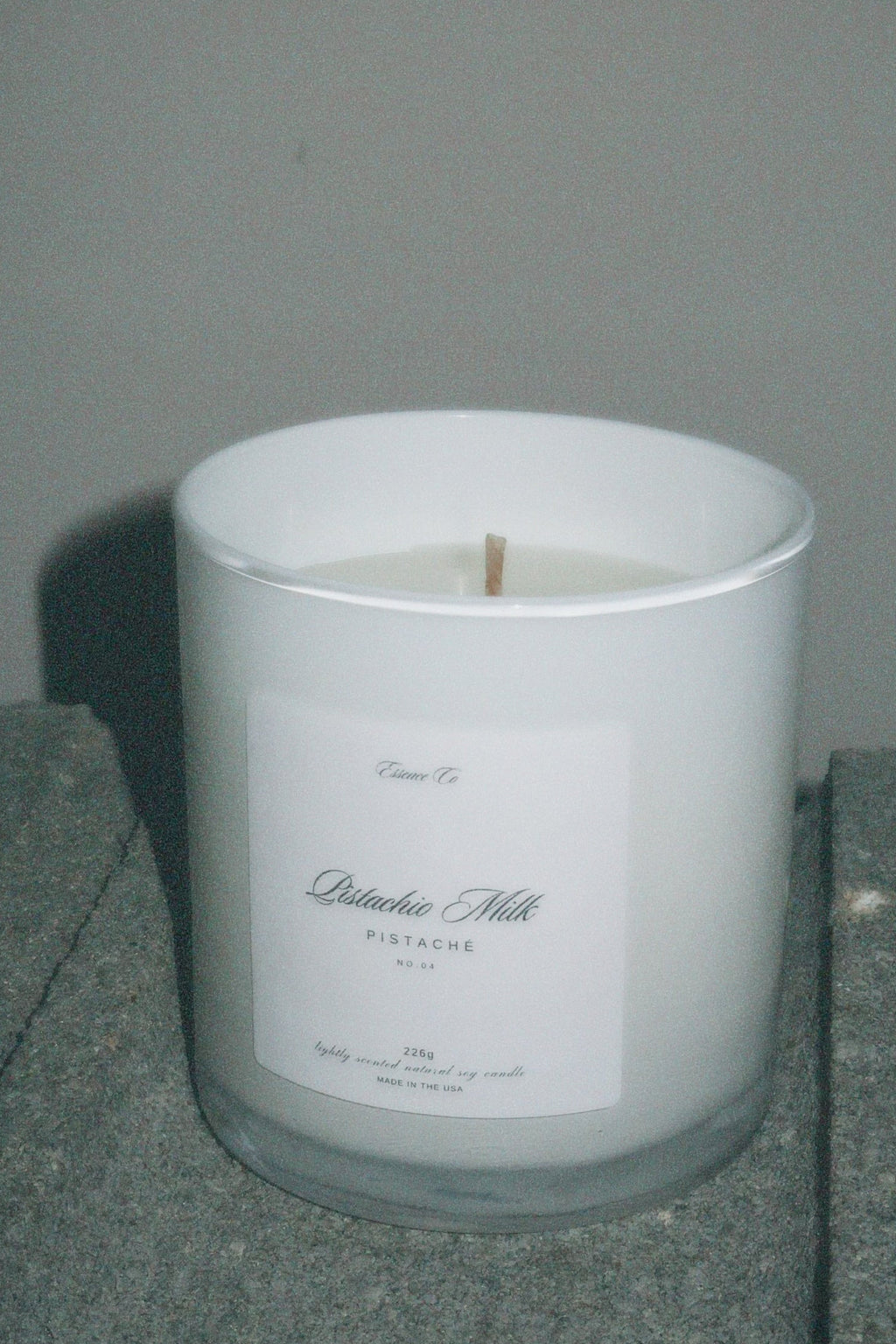White candle in a glass container with a label on a gray surface against a gray background