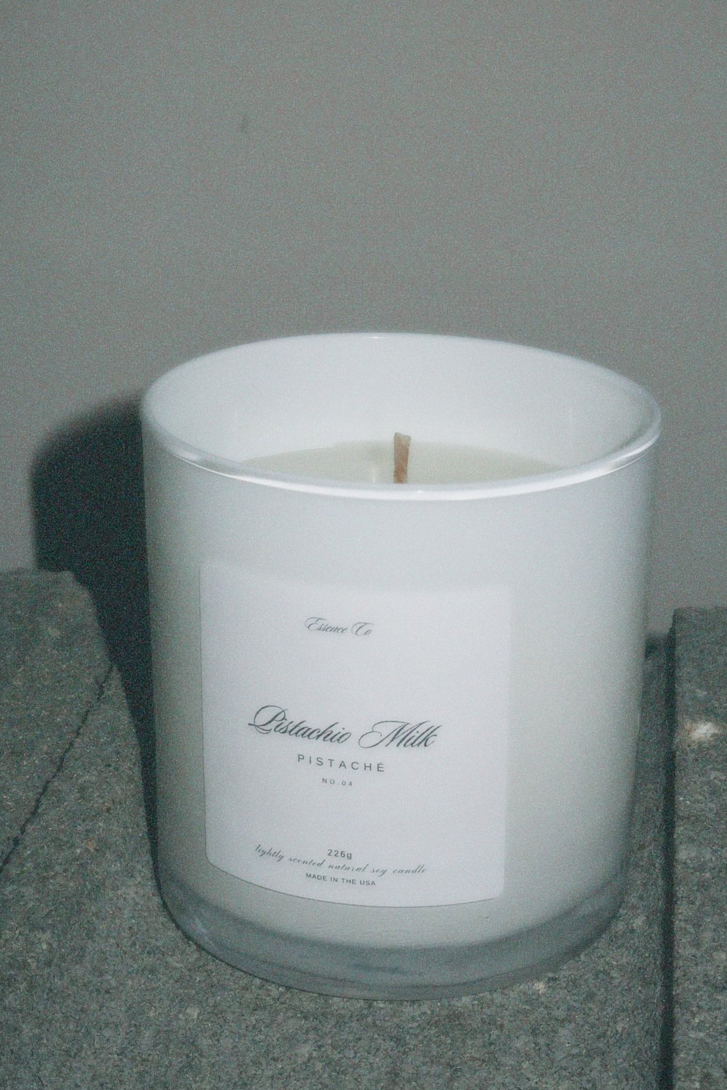 White candle in a glass container with a label on a gray surface against a gray background